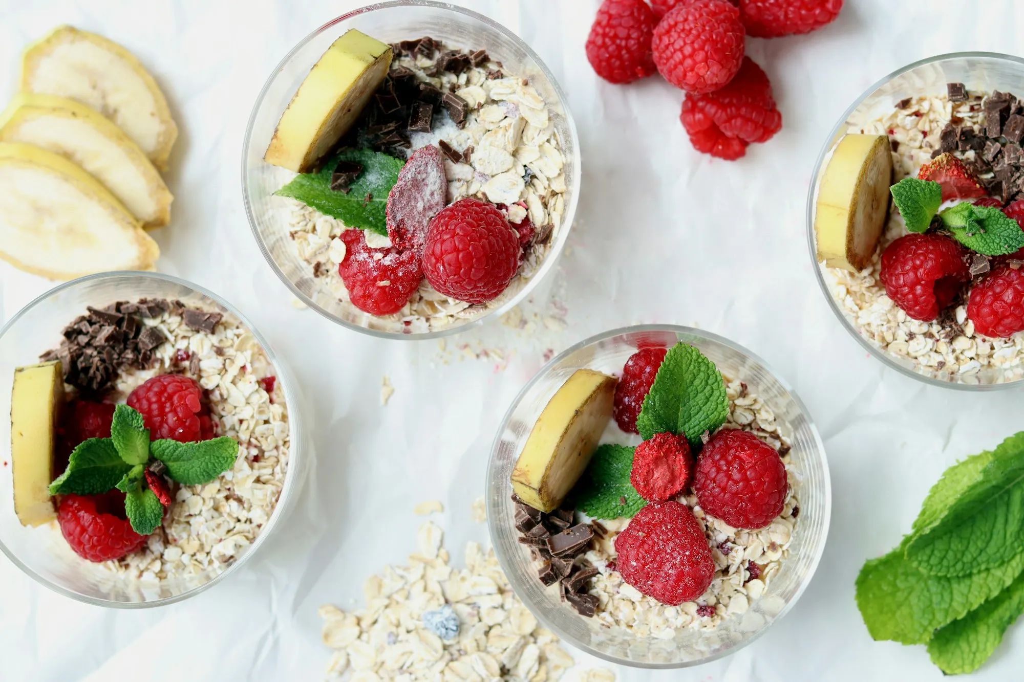 Copos com aveia, iogurte, banana, framboesas e chocolate vistos de cima